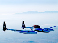 Global Flyer flying high with misty mountains in distance.